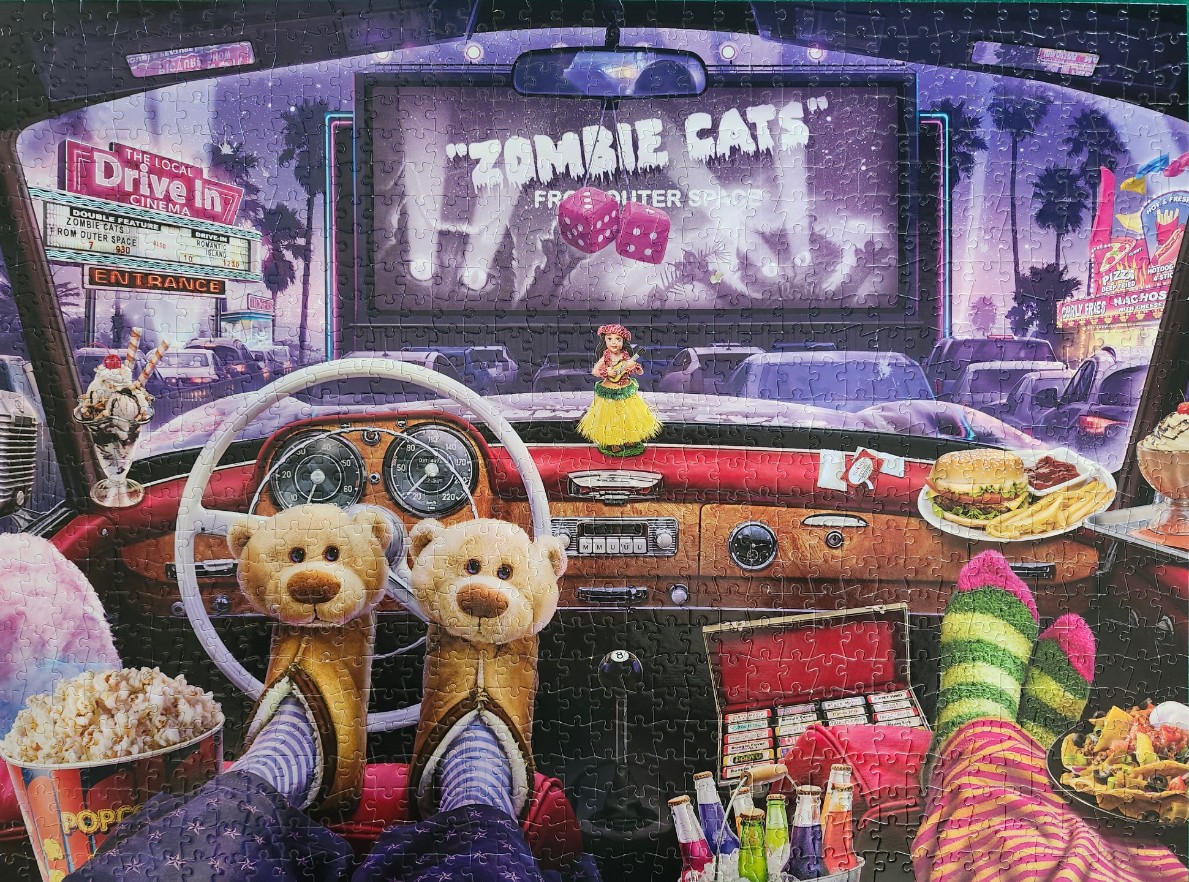 POV shot from inside a retro car at a drive-in theater showing a Zombie Cats horror movie.