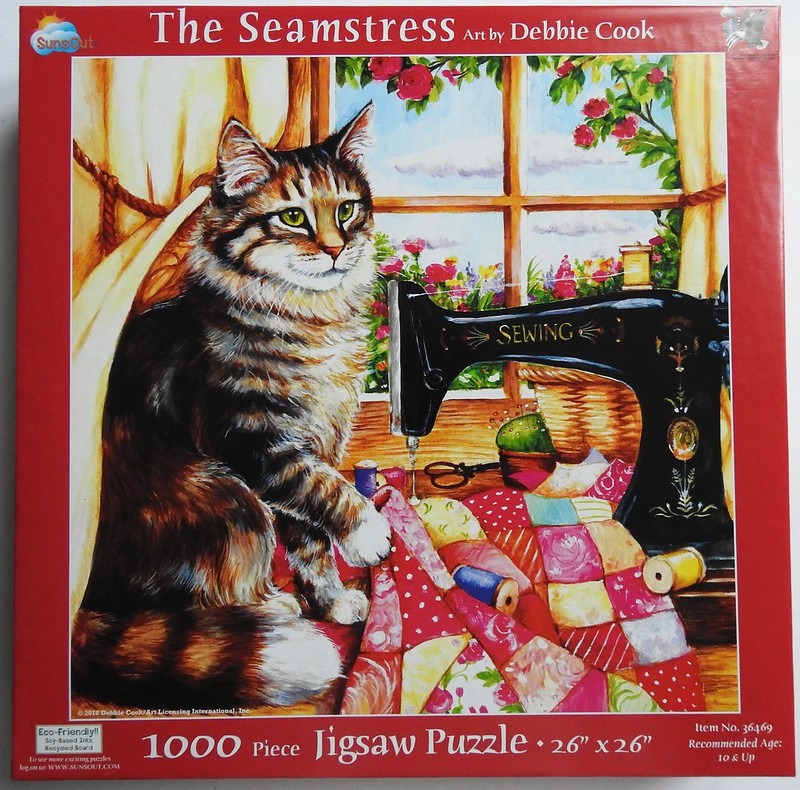 A fluffy tabby cat sits next to a vintage black sewing machine on a quilt in front of a sunny garden window.