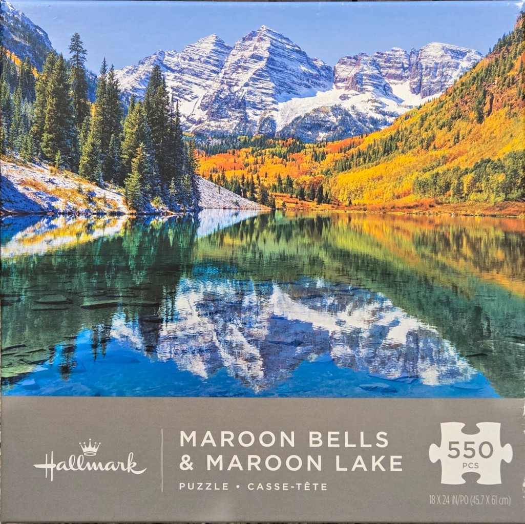 A photograph of the Maroon Bells mountains reflecting in the calm waters of Maroon Lake during autumn.