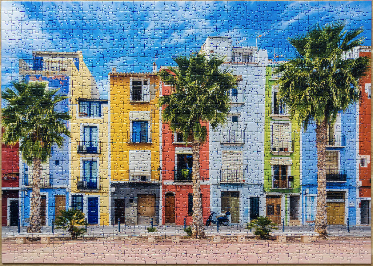 A row of colorful Mediterranean-style buildings with palm trees under a bright blue sky.
