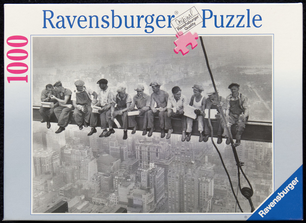 Black and white photograph of eleven ironworkers sitting on a steel beam high above a city.