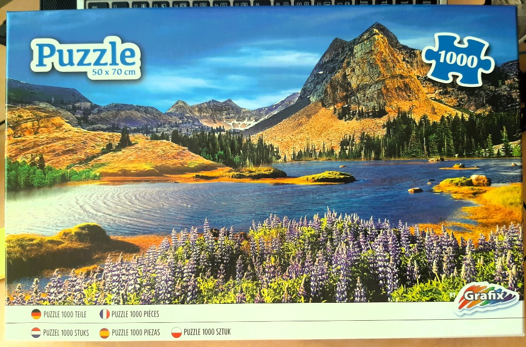 A scenic mountain landscape featuring a blue lake and foreground lupine flowers under a sunny sky.