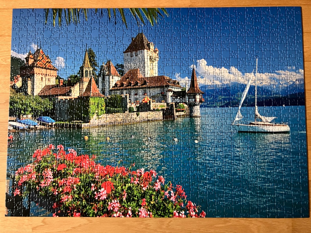 Chillon Castle on Lake Geneva with flowers in the foreground and a sailboat on the water.