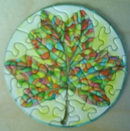 A circular stained-glass style illustration of a vibrant, multicolored maple leaf against a pale yellow background.