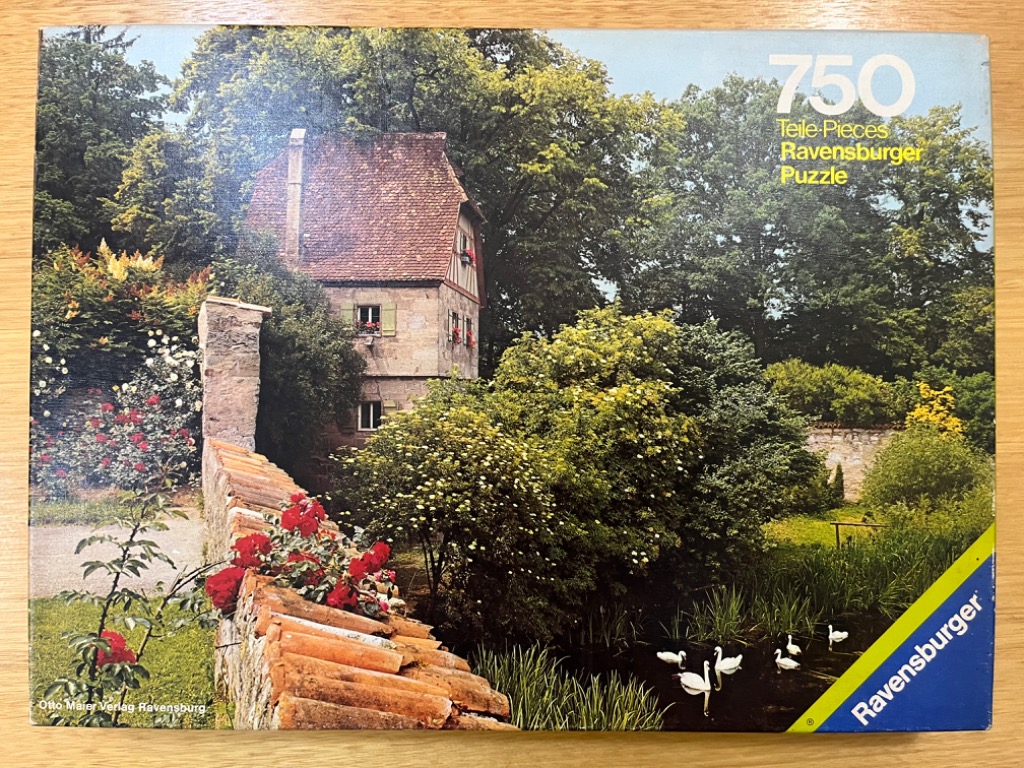 A peaceful European stone house with red-tiled roof and red roses, set behind a garden wall by a pond with white swans.