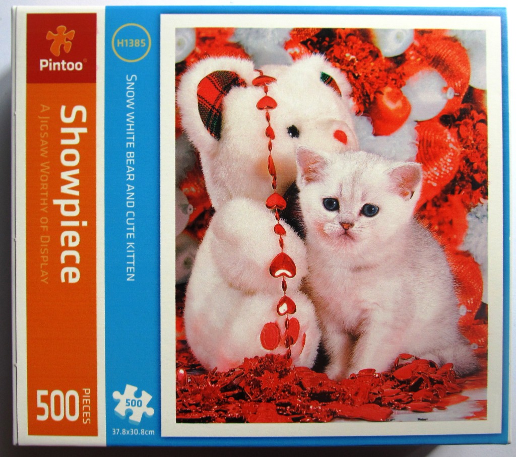 A white teddy bear sitting next to a small, fluffy white kitten surrounded by red holiday ornaments.