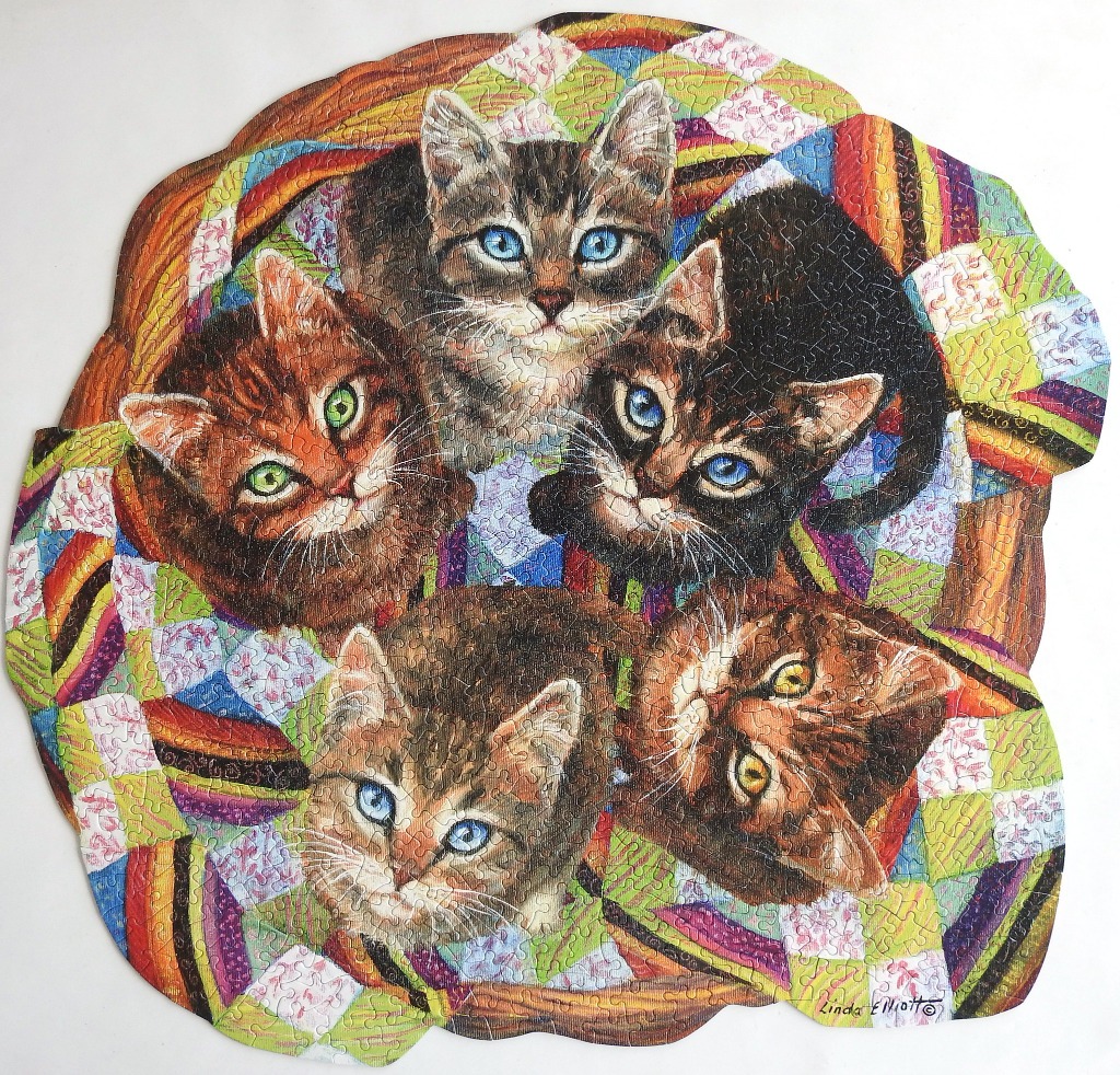 An illustration of four fluffy kittens gathered together on a colorful, patterned quilt.