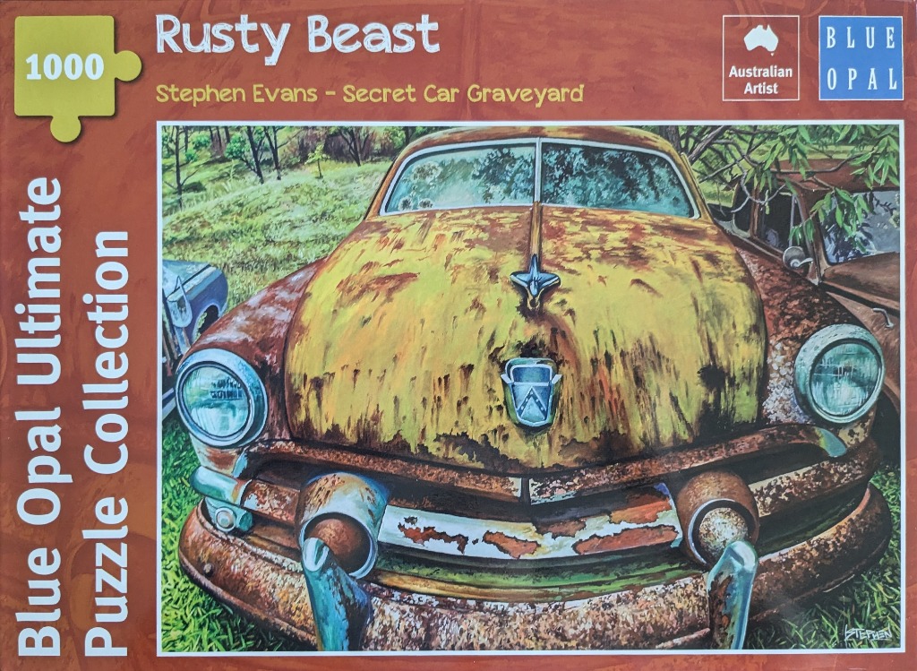 A vintage, heavily rusted car abandoned in a grassy, wooded area.