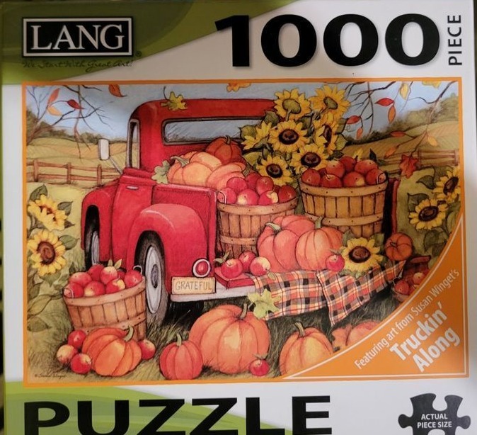 A red vintage pickup truck parked in an autumn field filled with pumpkins, sunflowers, and baskets of apples.
