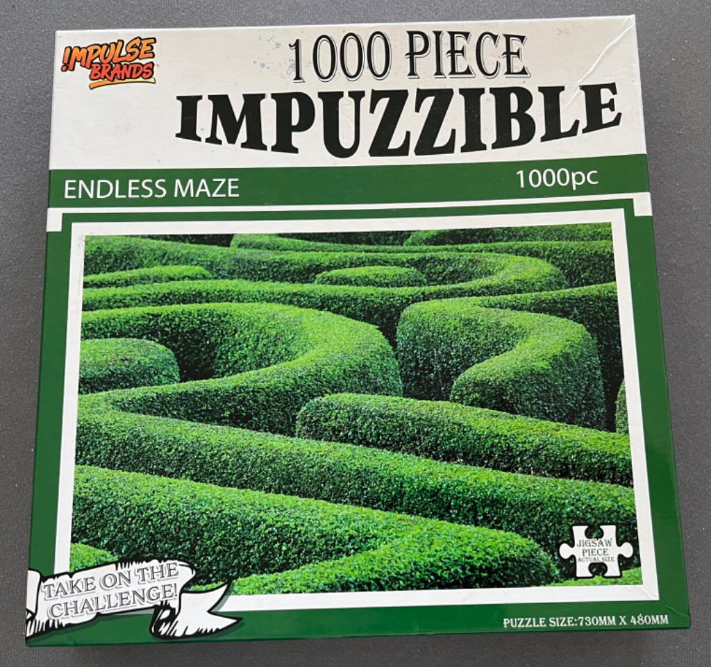 A close-up photograph of a lush green hedge maze with winding, repetitive patterns.