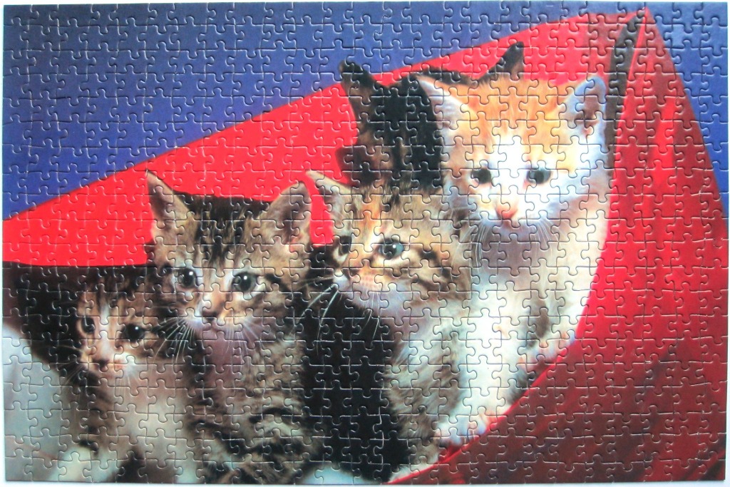 A group of four kittens peering from behind a vibrant red fabric against a dark blue background.