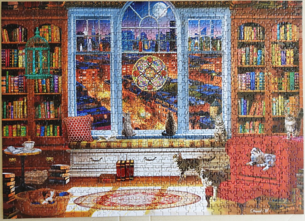 A cozy home library at night with cats and a view of a city skyline through a window.