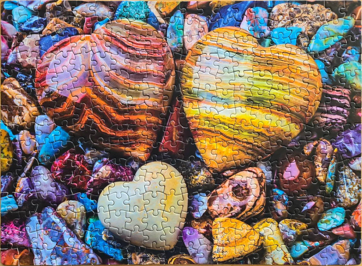 Three heart-shaped polished stones resting on a background of various colorful gemstones.