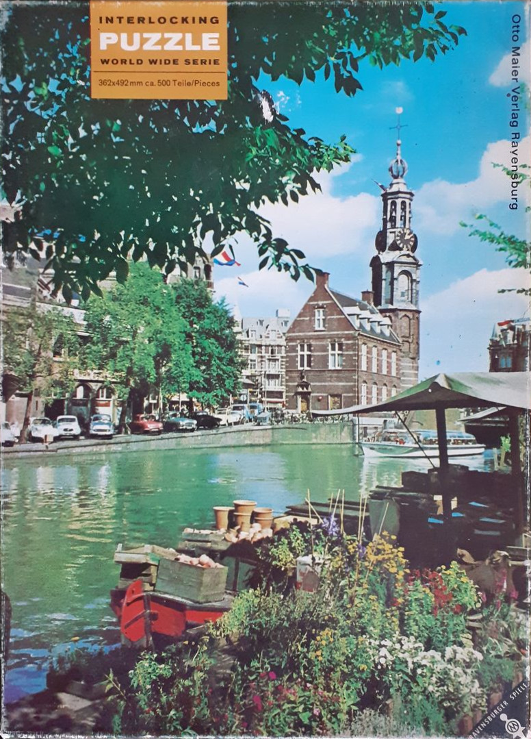 A scenic view of a canal in Amsterdam featuring a tall church tower and a flower stall in the foreground.