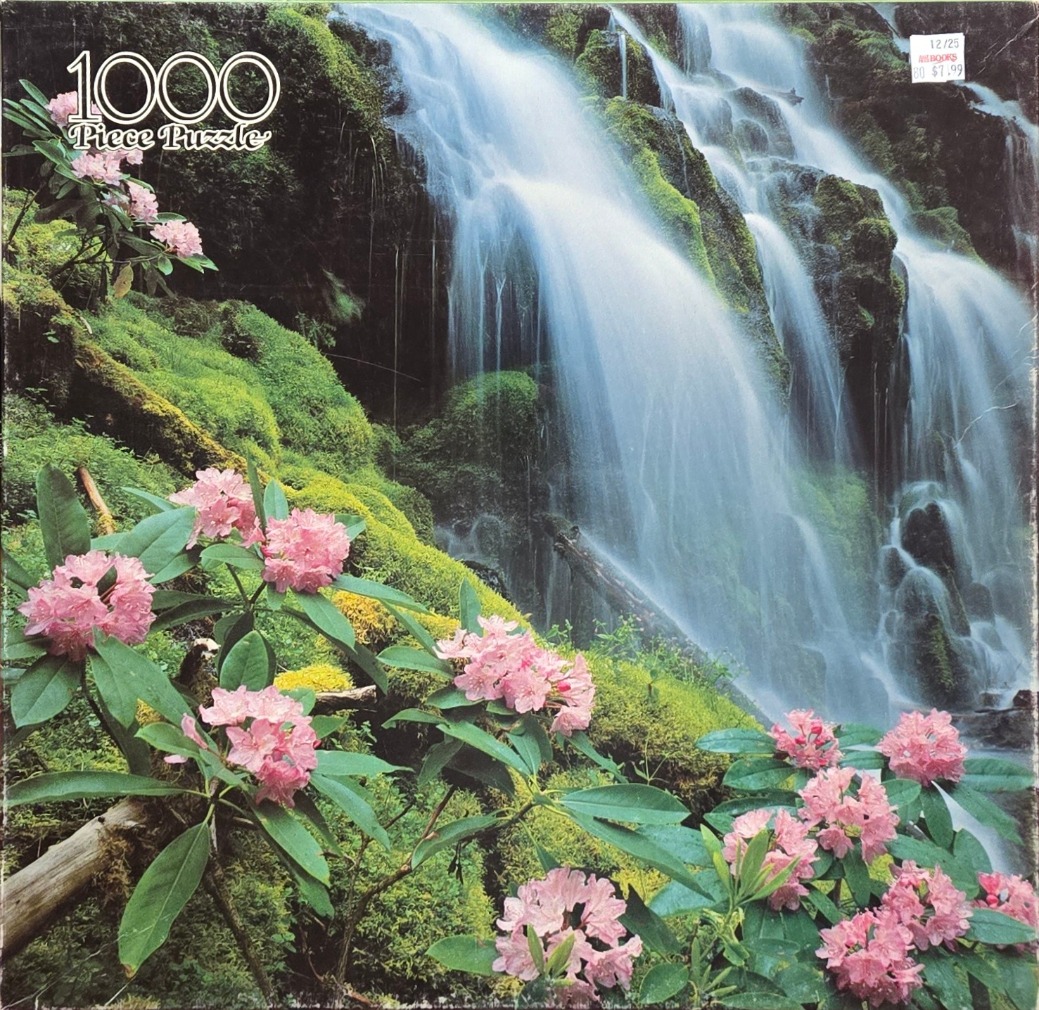 A lush, mossy waterfall cascading over rocks behind a foreground of blooming pink rhododendron flowers.