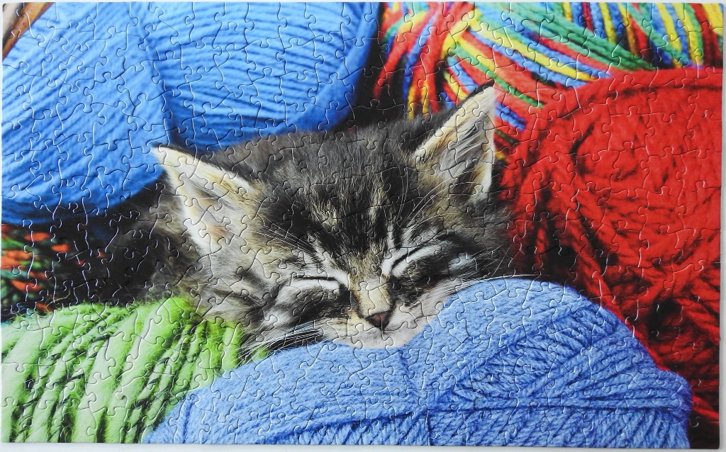 A fluffy tabby kitten sleeping nestled among several large balls of brightly coloured yarn.