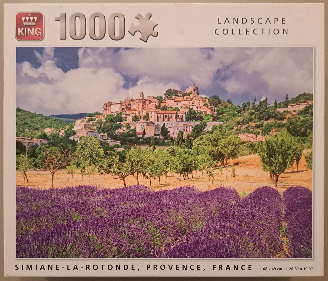 A scenic photograph of a lavender field in front of a hillside village in Simiane-la-Rotonde, Provence, France.