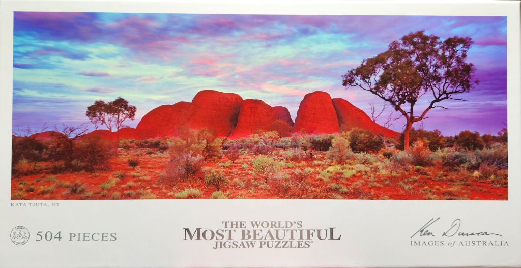 A panoramic photograph of the bright red rock domes of Kata Tjuta under a vivid sunset sky.