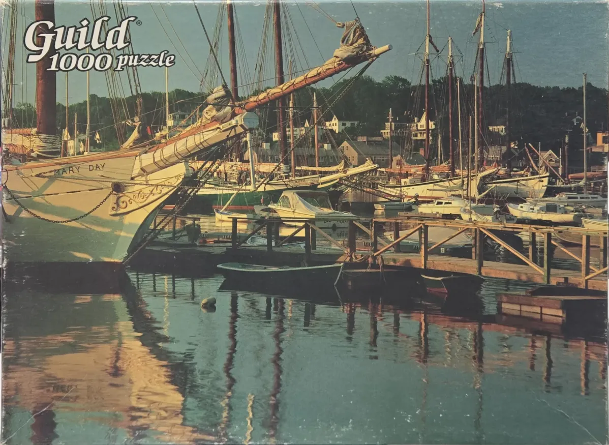 A vintage photograph of sailing schooners and small boats docked in a calm harbor at twilight.
