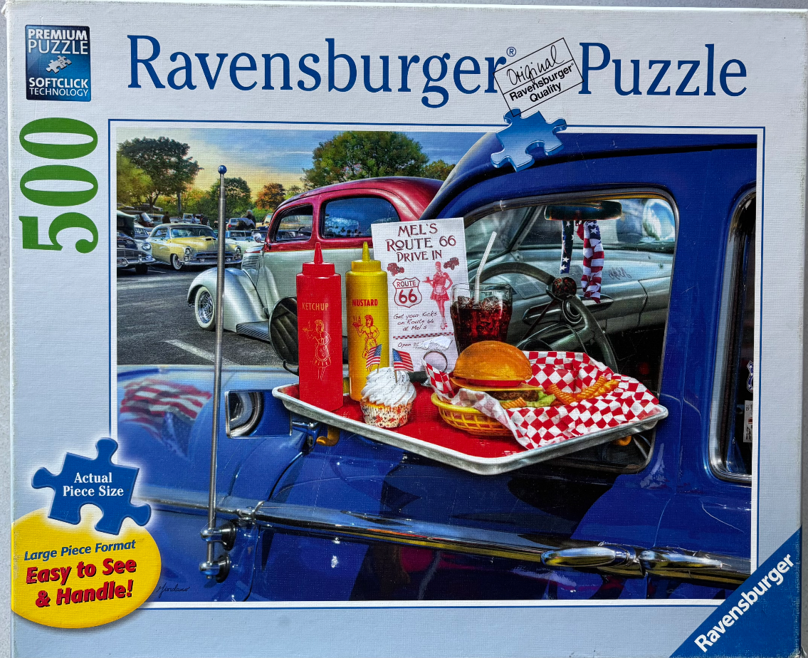 A drive-in restaurant tray of food resting on the window of a shiny blue vintage car at a car show.