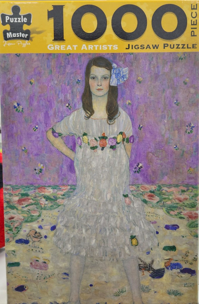 A girl with a blue hair ornament in a light grey ruffled dress standing against a purple floral backdrop.