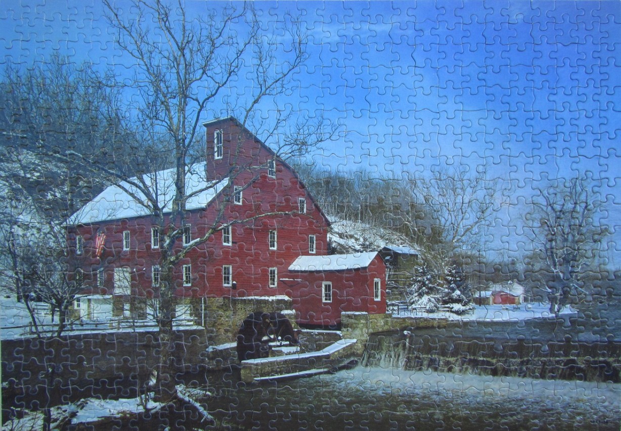 A red historic grist mill by a frozen river in a winter landscape.