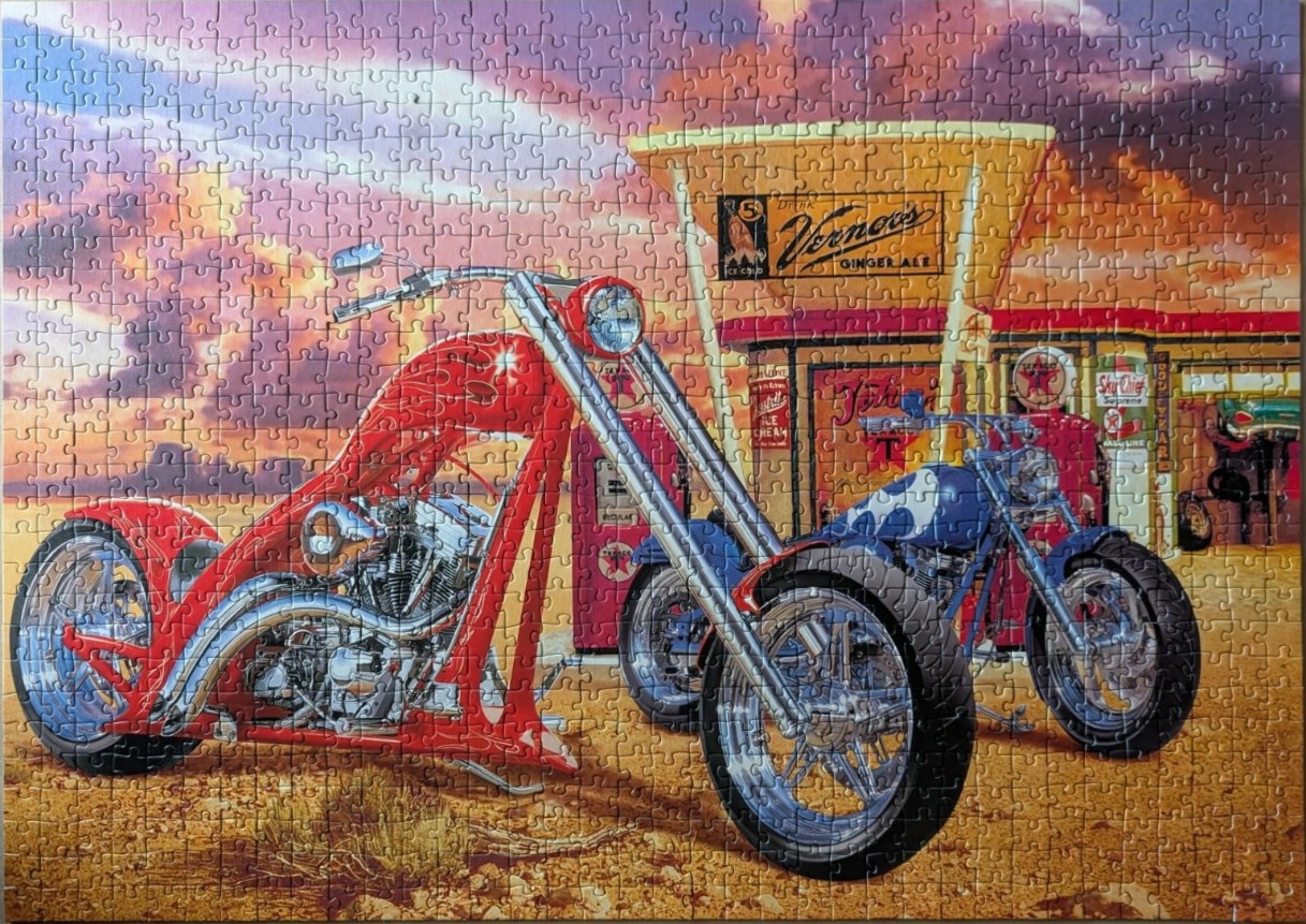 Two custom motorcycles parked at a vintage gas station during a sunset.