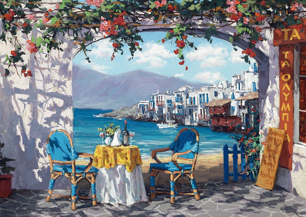 A sunny seaside patio overlooking a white-washed Greek village with blue shutters and a clear blue sea.