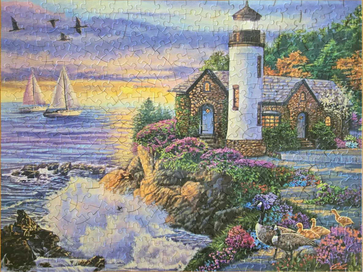 A lighthouse by a coastal cliff at sunset with sailboats on the water and geese in the foreground.