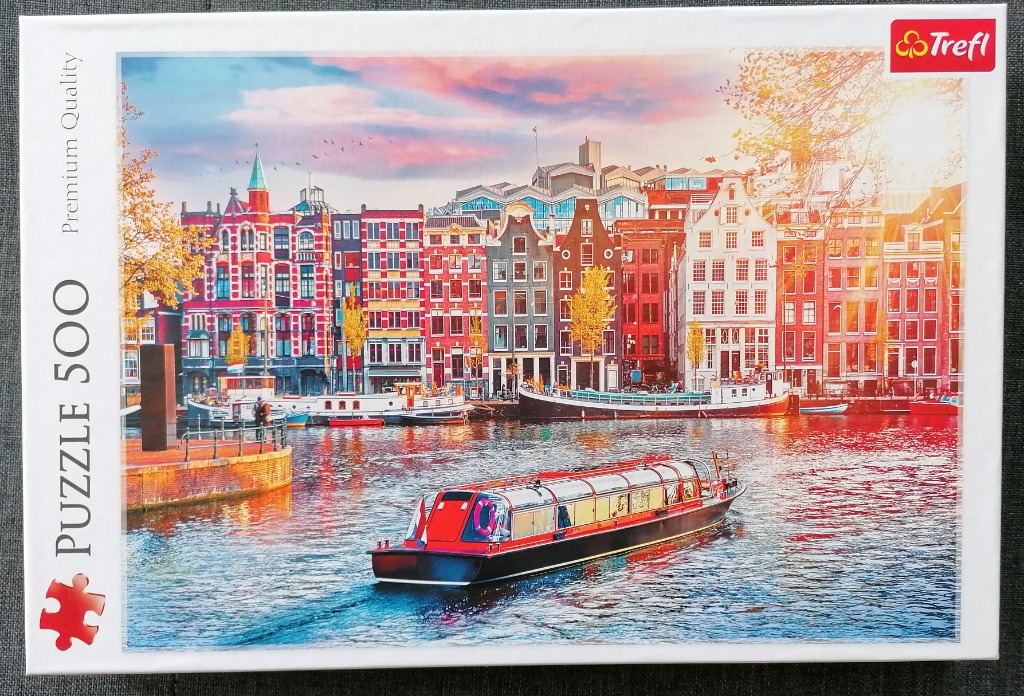 A scenic view of a canal in Amsterdam featuring historic Dutch buildings, houseboats, and a sleek modern tour boat.