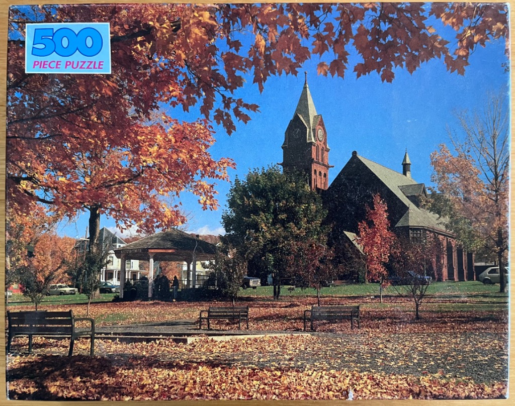 A photograph of a New England town square in autumn, featuring a gazebo, a historic brick church, and colorful foliage.