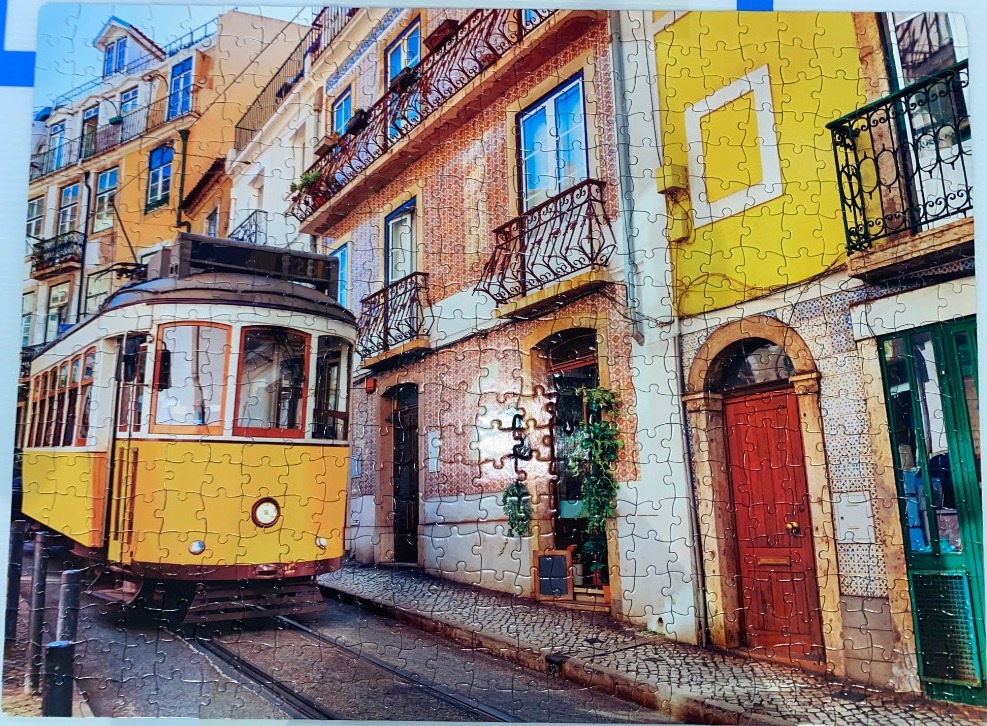 A vintage yellow tram traveling along a narrow street lined with traditional tiled buildings in Lisbon.