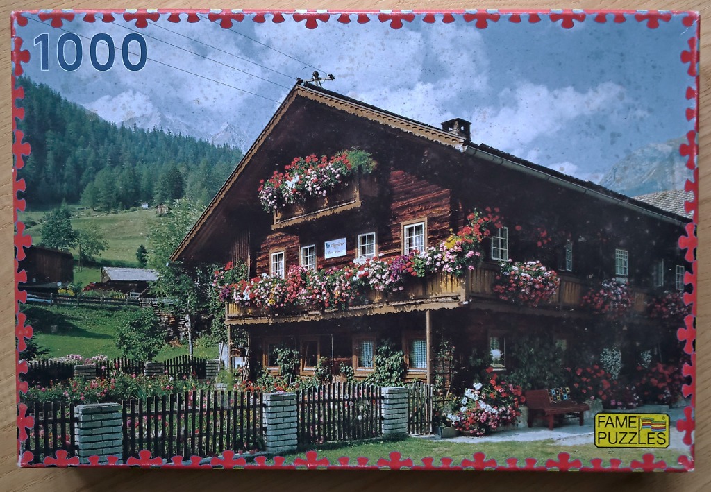 A photograph of a traditional wooden alpine chalet adorned with overflowing flower boxes against a mountain backdrop.