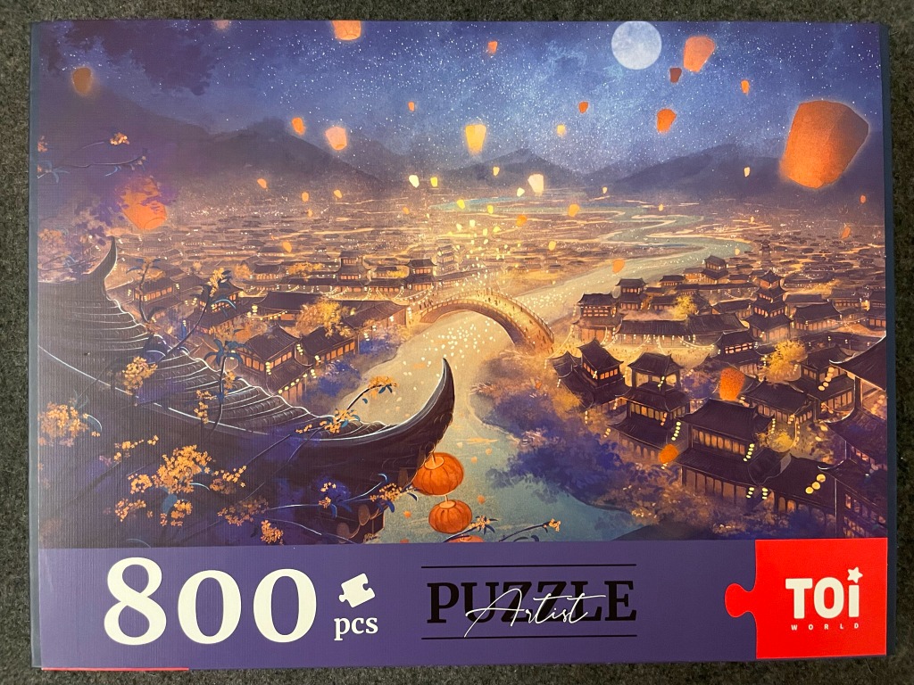 An illustration of an ancient Asian town at night, illuminated by numerous glowing floating lanterns and a full moon.