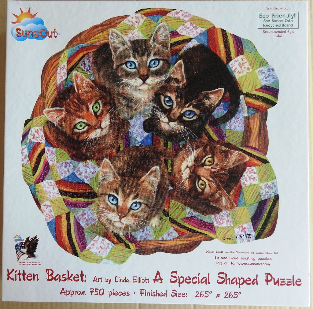 Five kittens looking up from inside a woven basket lined with a colourful quilted blanket