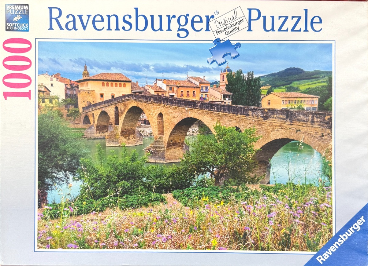 A stone arched bridge spanning a calm river with a historic village in the background.