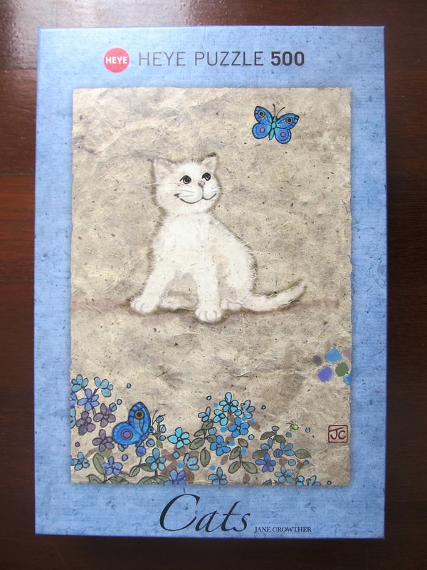 A whimsical illustration of a small white kitten sitting among blue flowers and butterflies on textured beige paper.