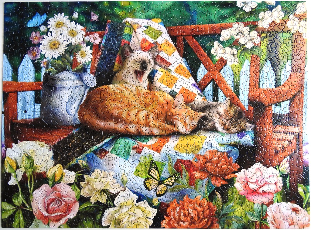A Siamese and tabby cat resting on a quilt-covered bench surrounded by vibrant flowers and a butterfly.