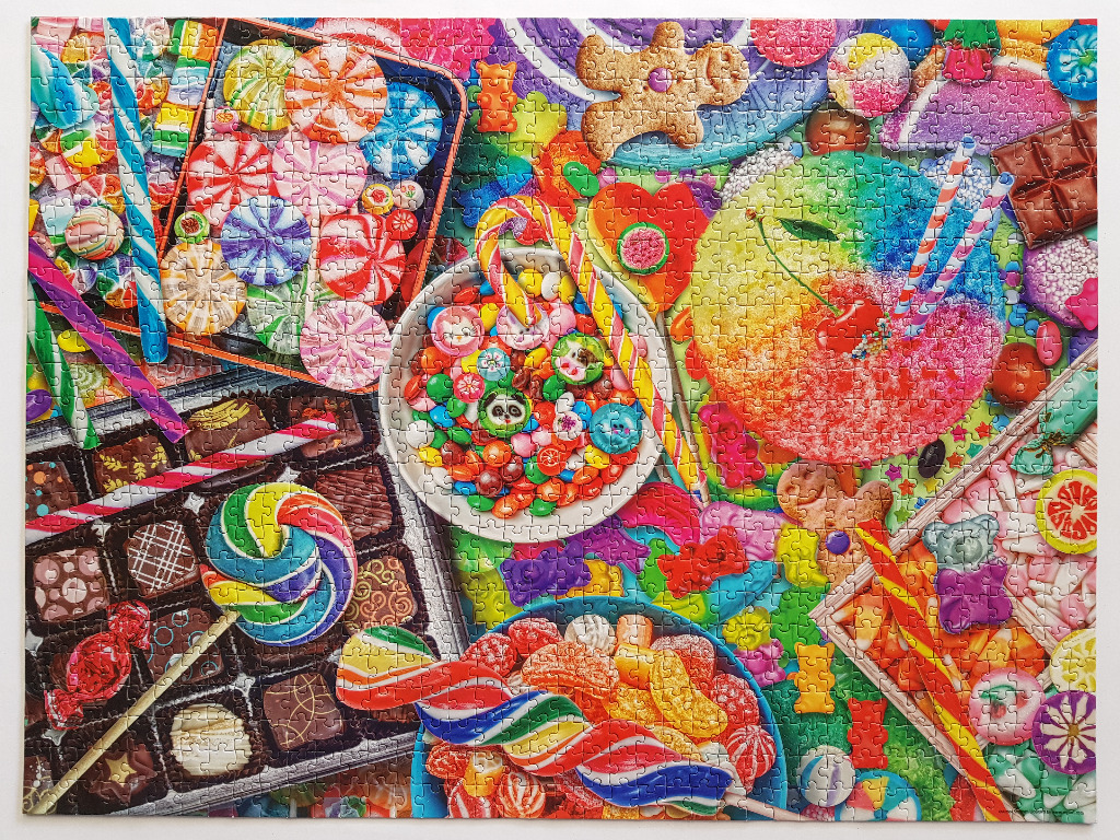 A vibrant, overhead display of various candies, chocolates, sweets, and a rainbow-colored shaved ice treat.