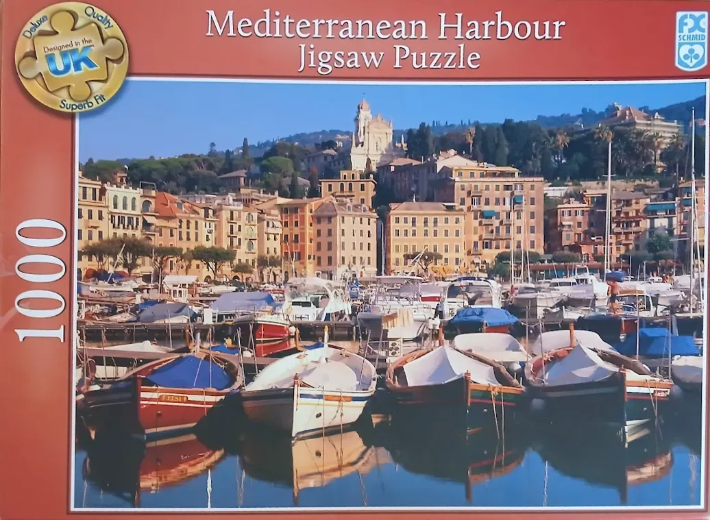 A sunny Mediterranean harbor with colorful boats and traditional buildings at the base of a forested hillside.