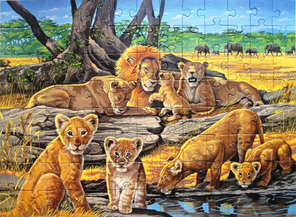 A pride of lions resting in an African savanna landscape with a herd of elephants in the distance.