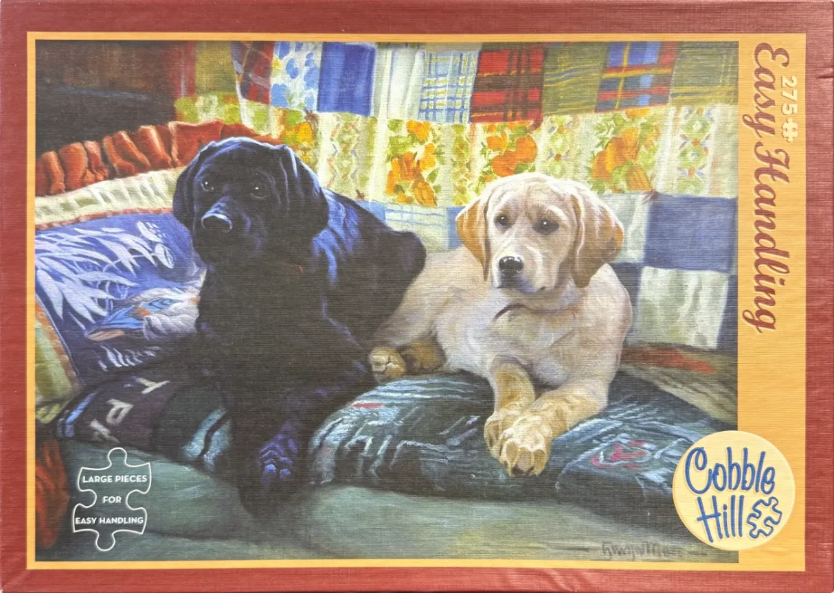 A painting of a black Labrador and a yellow Labrador sitting together on a cozy couch covered with a colorful patchwork quilt