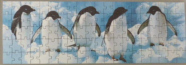 Five Adelie penguins standing on snow against a blue sky with clouds.