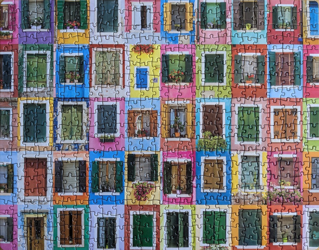 A grid of colorful windows on Mediterranean-style buildings in Burano, Italy.