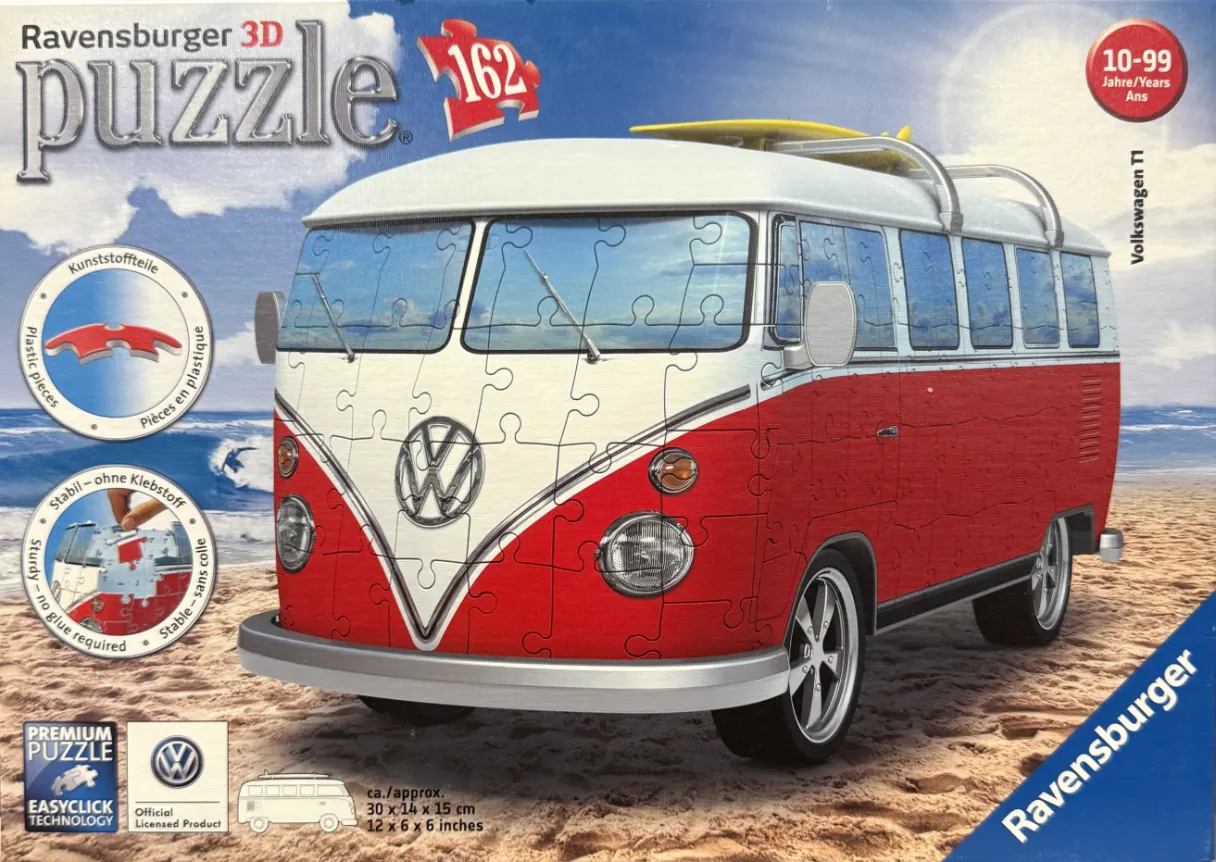 A red and white vintage Volkswagen T1 bus parked on a sandy beach.