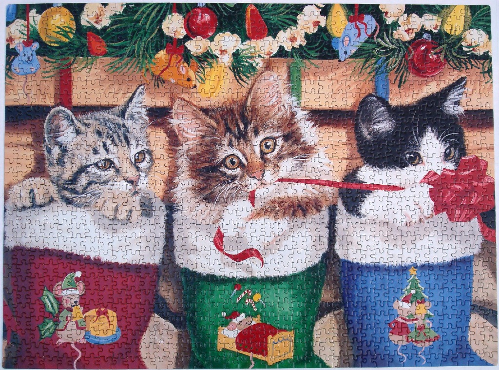 Three kittens sitting in individual Christmas stockings hanging in front of a fireplace mantel.