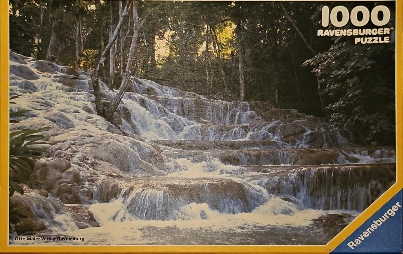 A lush, tiered tropical waterfall cascading over layered light-colored rocks in a forest setting.
