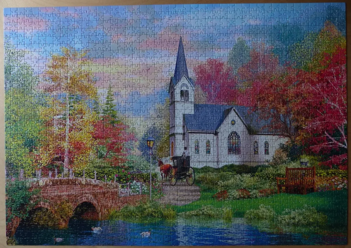 A peaceful autumn scene featuring a white church, a stone bridge, and a horse-drawn carriage by a pond.