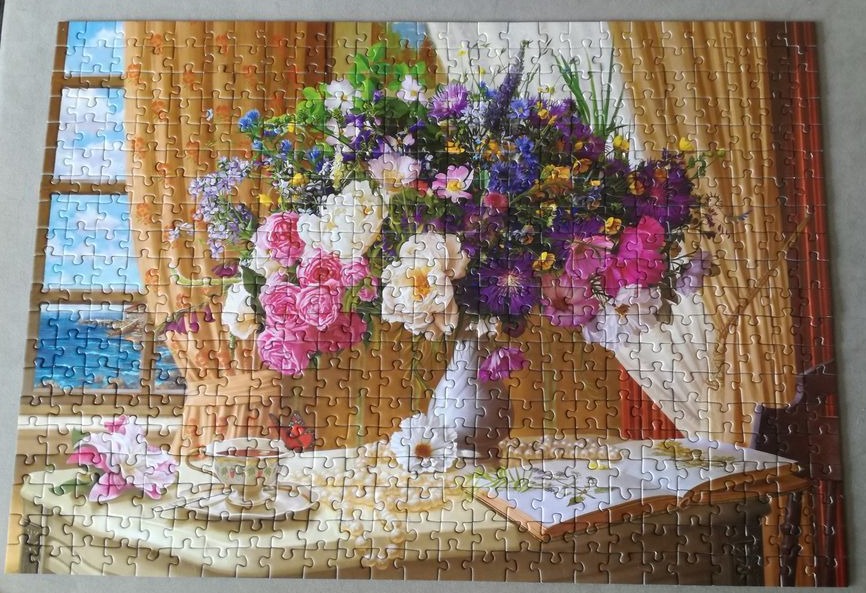 A lush bouquet of wildflowers and roses in a white vase sits on a table by a window with a seaside view.