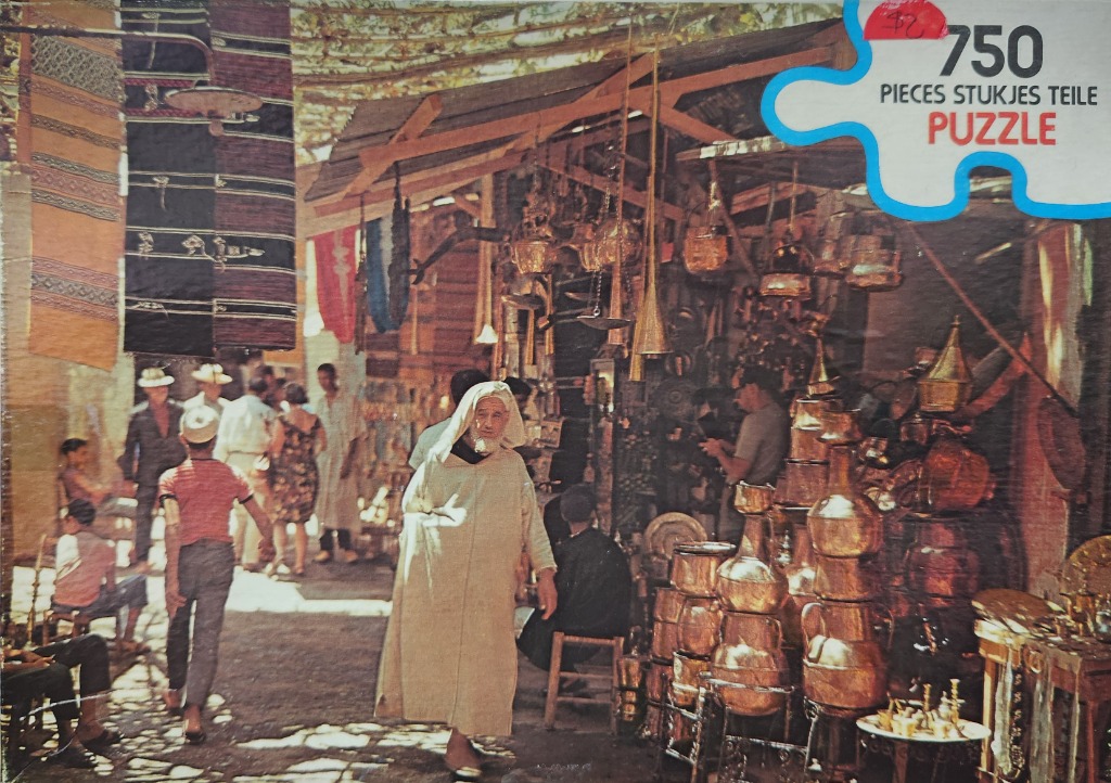 A street scene in a North African market featuring a man in a djellaba walking past stalls filled with copper wares.